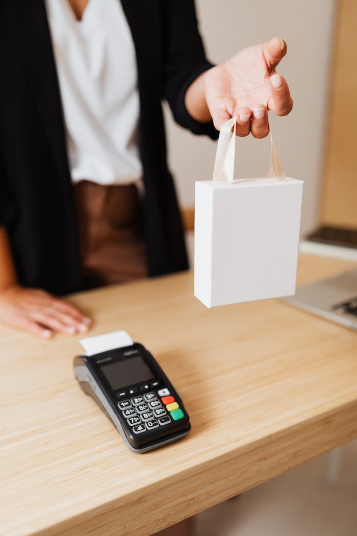 Services Close-up of shopper's hand holding a bag next to a payment terminal on a wooden counter.